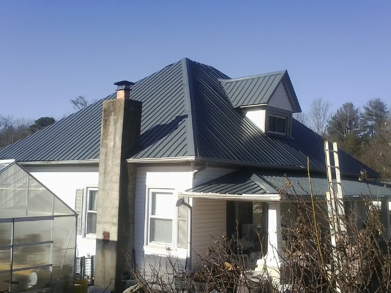 Dark blue standing seam metal roof on a white farmhouse with dormer — Slate & Tile Roof Repair by Roofing Brothers in Burbank