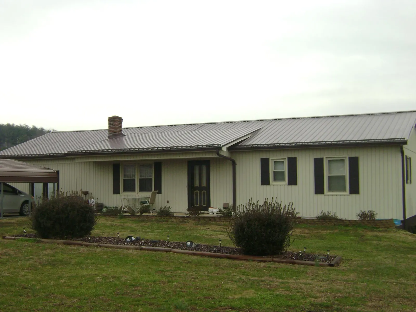 Brown metal roof on a cream sided ranch home with a brick chimney in Burbank